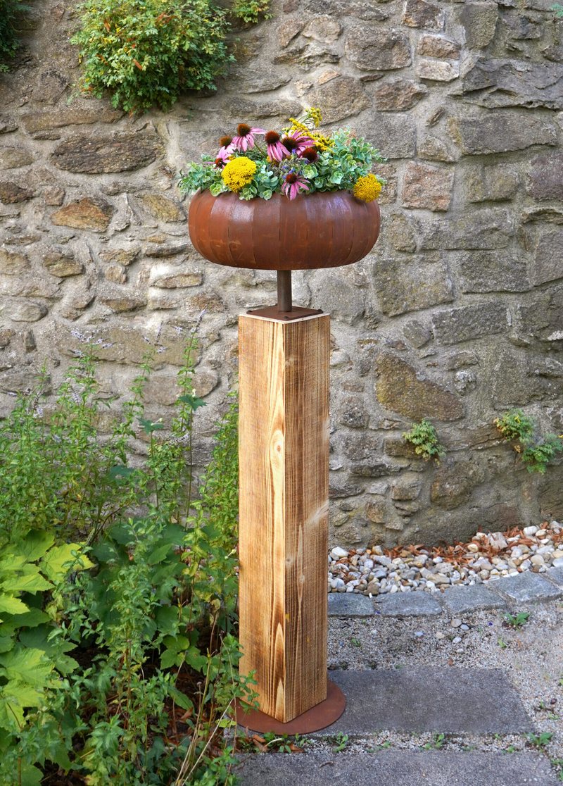 Holzsäule mit Pflanzschale aus Stahl mit Edelrost, bepflanzt, vor einer Natursteinmauer